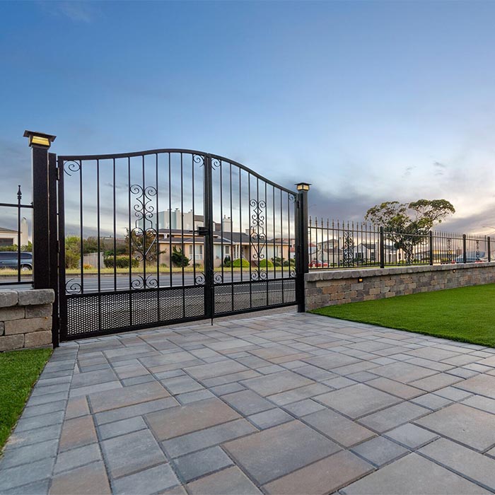 Beautiful iron gate and fence with a stone pavers driveway.